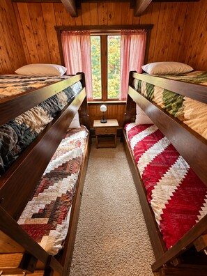 A room with two bunk beds, a small table with a lamp, and a window with curtains.