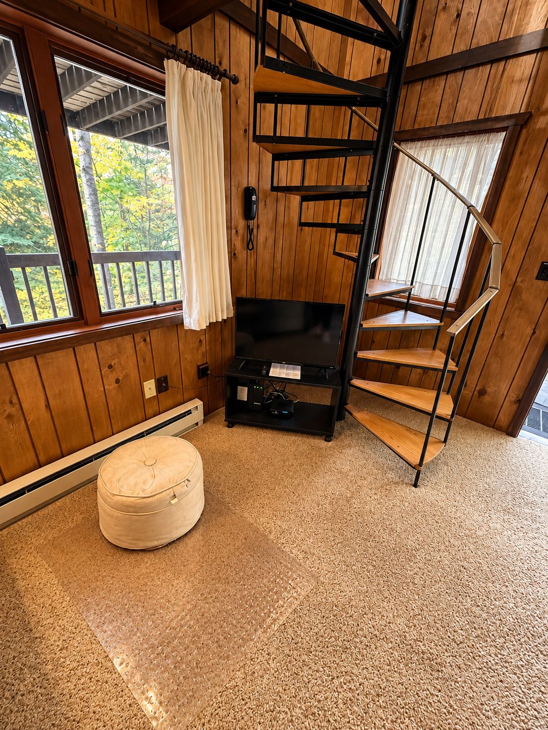 Un intérieur en bois avec un escalier en colimaçon, un téléviseur à écran plat et un téléphone fixé au mur.