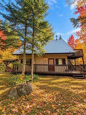 A cabin with a metal roof, wooden deck, and a staircase leading to a porch.
