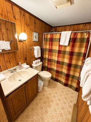 A bathroom with wooden paneling, a sink, a toilet, and a shower curtain.