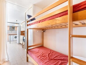 Quarto com beliche e cozinha ao fundo.