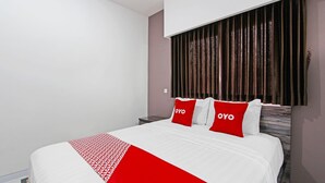 Una camera d'albergo con un letto grande, due cuscini con la scritta "OYO", una coperta a letto rossa e bianca e una testiera in legno.