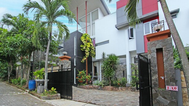 Una casa moderna a due piani con facciata in pietra, un cancello nero e una combinazione di colori rosso e bianco.