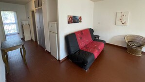 Ein Zimmer mit einer Couch, einem kleinen Tisch, einem Kühlschrank und einem Sessel.