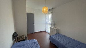 Ein Zimmer mit zwei Betten, einem Schreibtisch, einem Stuhl, einem Fenster mit Vorhängen und einer Pendelleuchte.