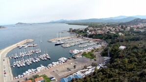 A marina with numerous boats docked, surrounded by a coastal town with buildings and hills in the background. - Holidays in Sardinia, apartment Arbatax (Arbatax)