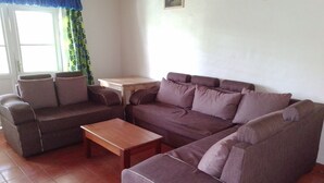 Sala de estar com um sofá marrom, uma mesa de centro de madeira e uma pequena mesa branca.