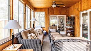 A cozy room with a wooden ceiling, large windows, a sofa, a chair, and a table with lamps. - Beach Access Steps Away, Hot Tub, Sleeps 12, Fire Pit (Union Pier)