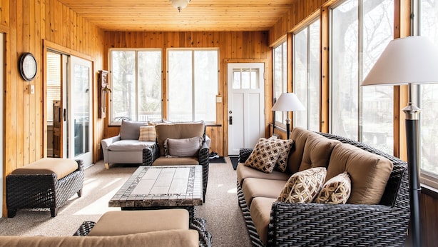 A cozy room with wooden walls and large windows, furnished with a sofa, chairs, and a coffee table. - Beach Access Steps Away, Hot Tub, Sleeps 12, Fire Pit (Union Pier)