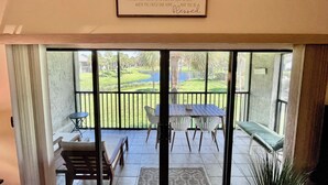A room with a sliding glass door leading to a balcony with a view of a golf course. There is a framed quote on the wall and a small table with chairs. - VDL 108 - Summer fun in the sun! (Saint Augustine)