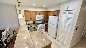 A kitchen with granite countertops, wooden cabinets, a white refrigerator, a microwave, an oven, and a sink. - VDL 108 - Summer fun in the sun! (Saint Augustine)
