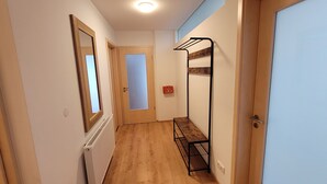 A narrow hallway with wooden flooring, a radiator, a metal bench, and a door with a mirror.