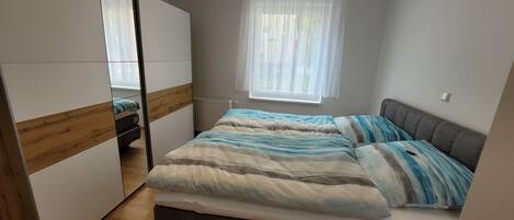 Une chambre à coucher avec un lit, une armoire, un radiateur et une fenêtre avec des rideaux.