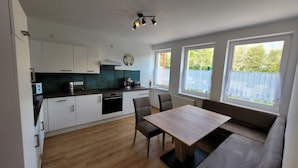 A modern kitchen with white cabinets, a wooden countertop, and a built-in oven. There is a dining area with a wooden table and two chairs.