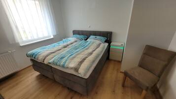 Quarto com cama, cadeira, mesa de cabeceira e janela.