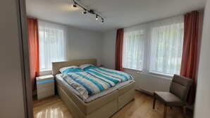 A bedroom with a bed, a chair, a nightstand, and a window with curtains.