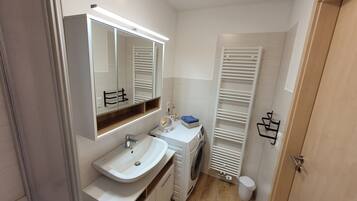 Un baño pequeño con lavamanos, espejo y lavadora incorporada.