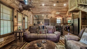 A cabin interior with a wooden ceiling, a sofa, a coffee table, and a kitchen area.