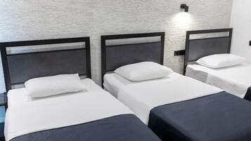 Ein Hotelzimmer mit drei Einzelbetten, jedes mit einem schwarzen Kopfteil und weißer Bettwäsche.