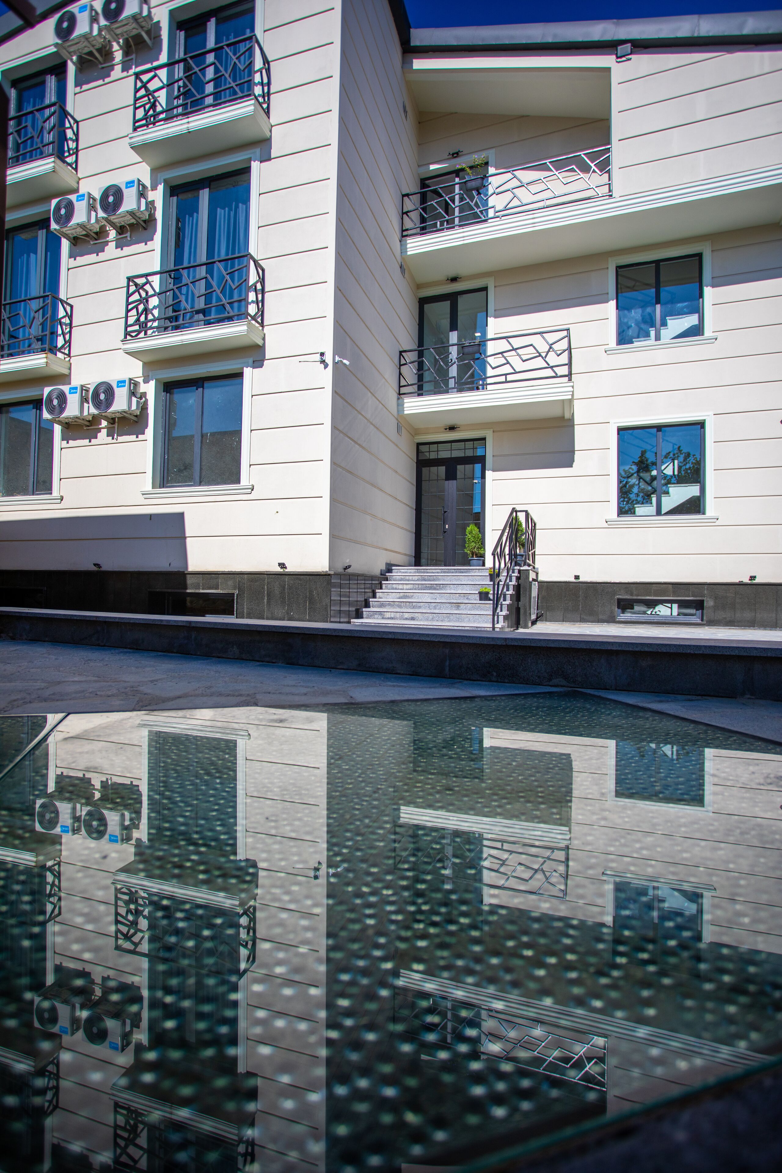 A modern building with multiple balconies, a pool area, and a clear reflection on the water.