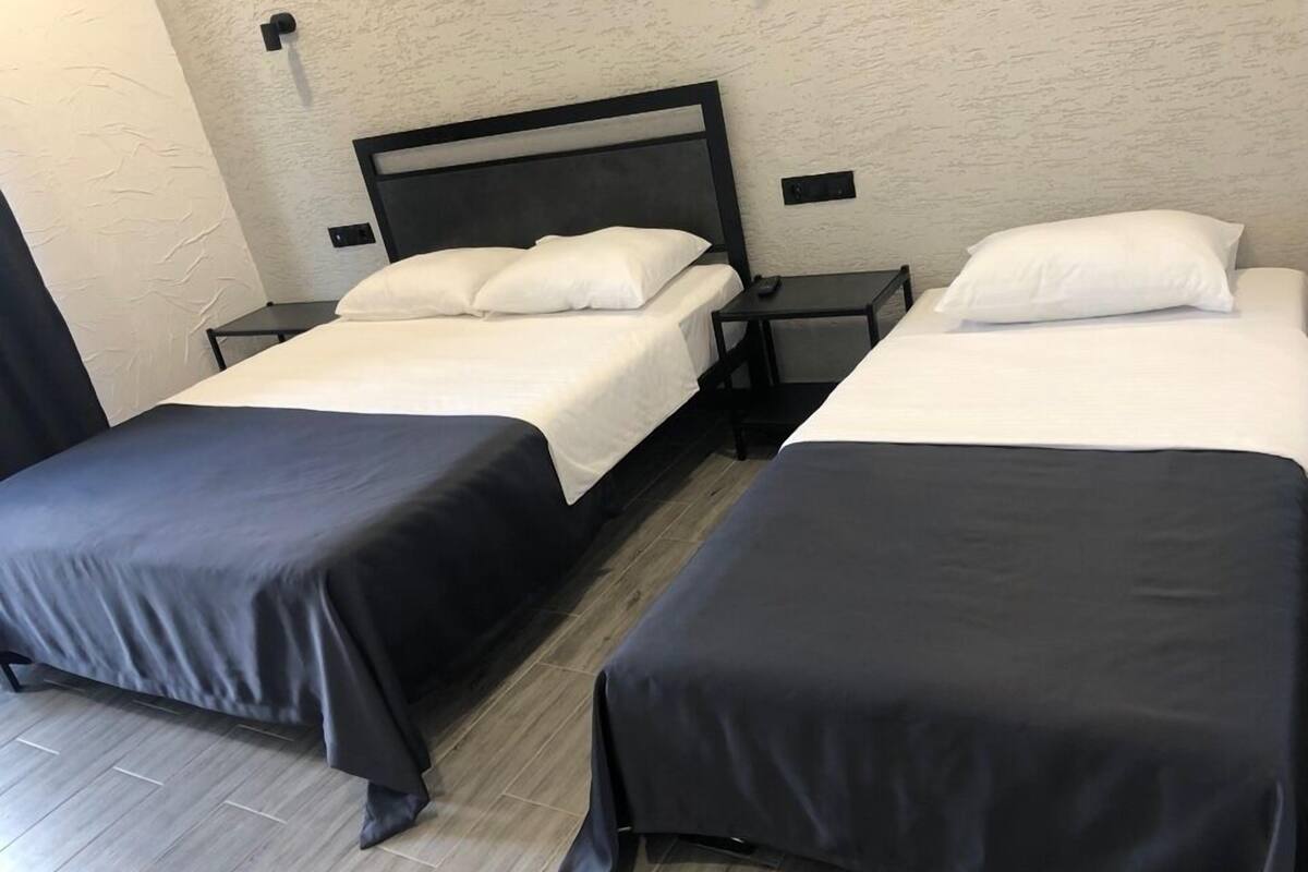 Une chambre avec deux lits simples, chacun recouvert d’une couverture noire et agrémenté d’oreillers blancs, ainsi qu’une table de chevet avec une télécommande.