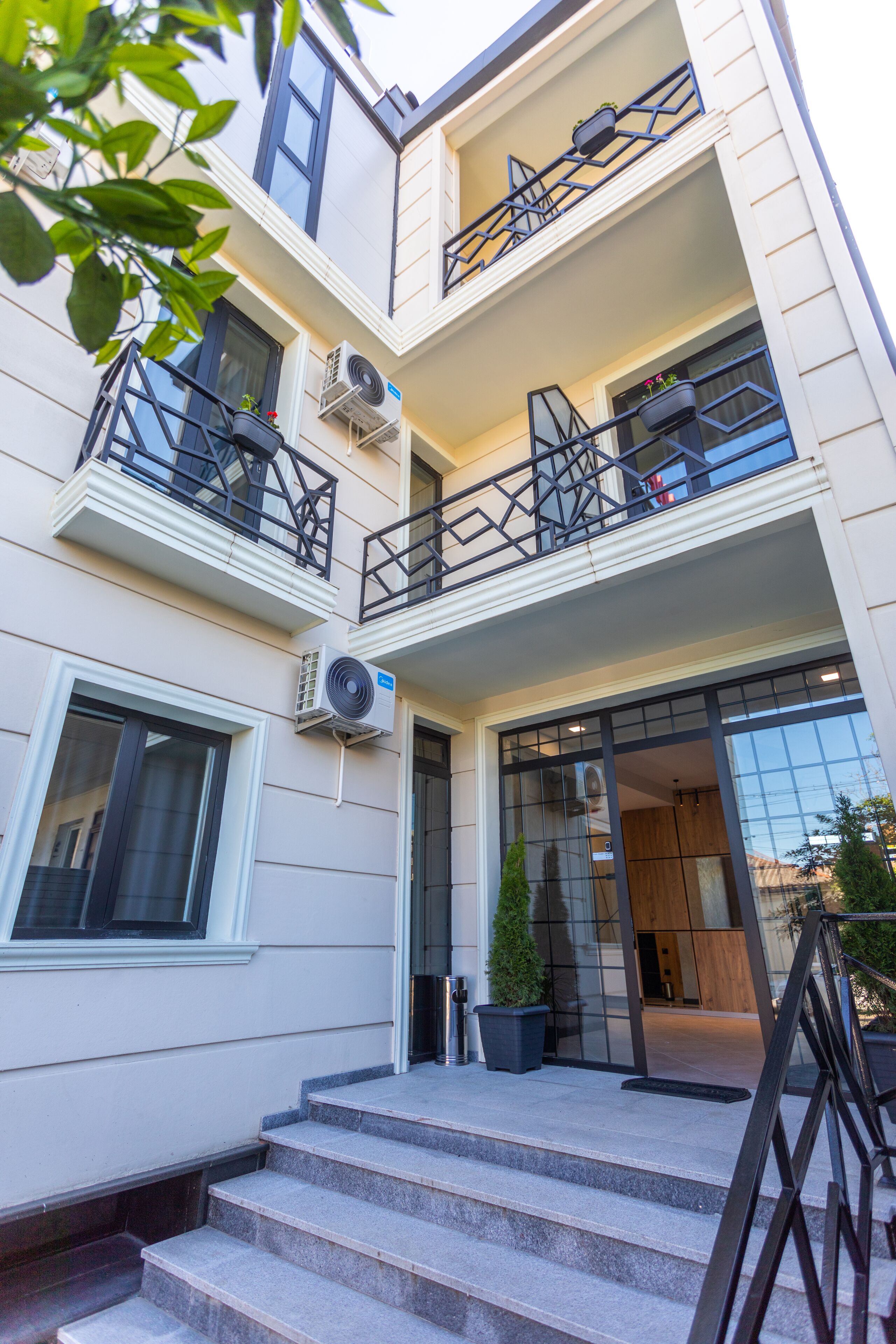 Un edificio moderno de varios pisos, con balcones con barandillas, unidades de aire acondicionado y una escalera que conduce a la entrada.