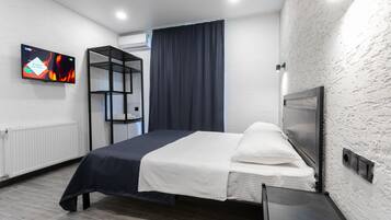 Een moderne hotelkamer met een bed, een aan de muur bevestigde televisie, een inbouwkast en een raam met gordijnen.