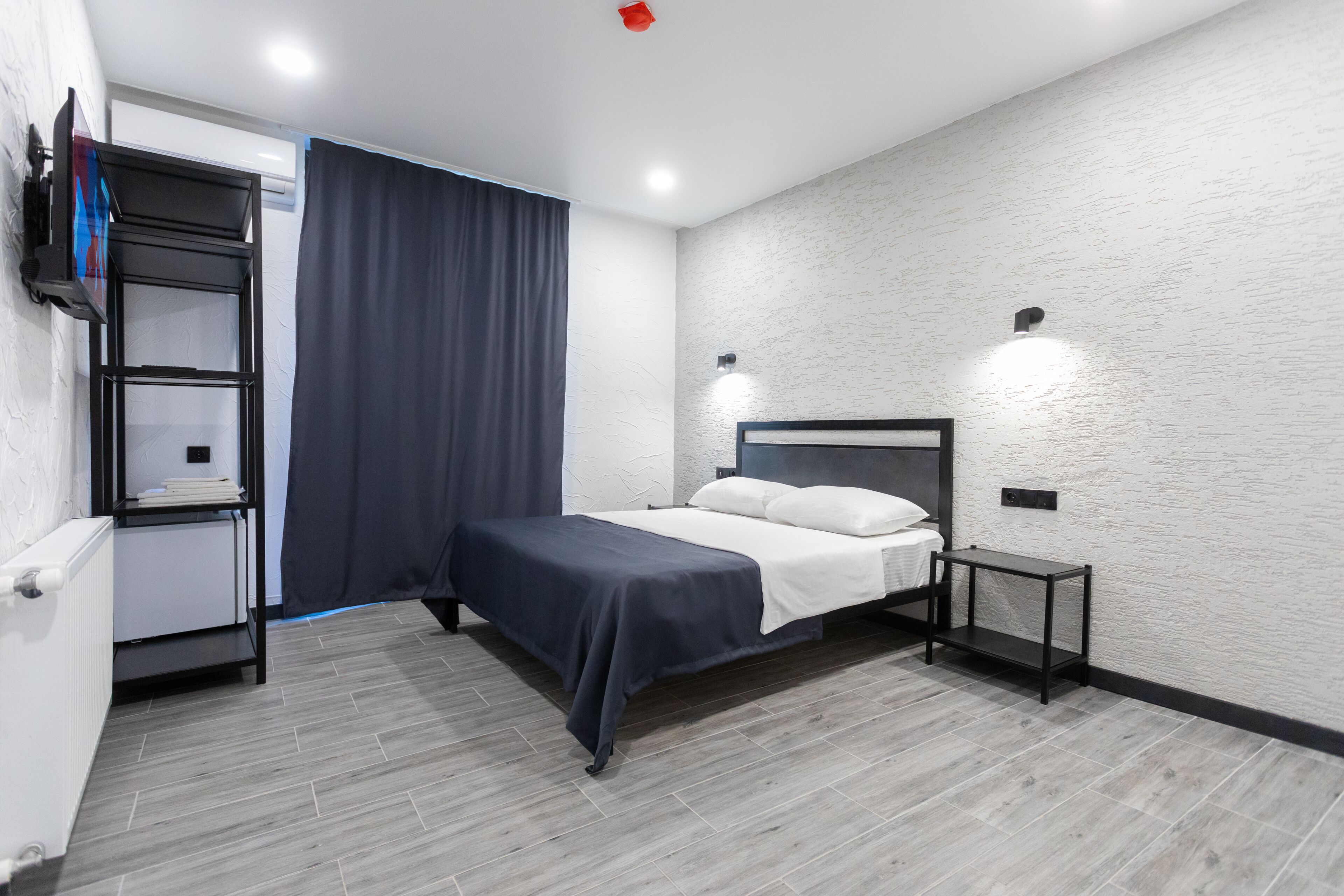 Un dormitorio moderno con cama, mesita de noche, estantería y televisor montado en la pared.