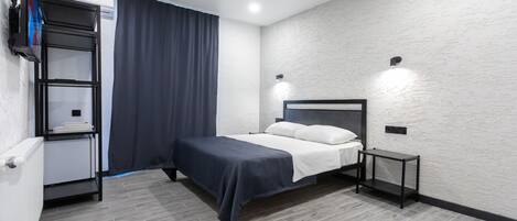 Un dormitorio moderno con cama, mesita de noche, estantería y televisor montado en la pared.