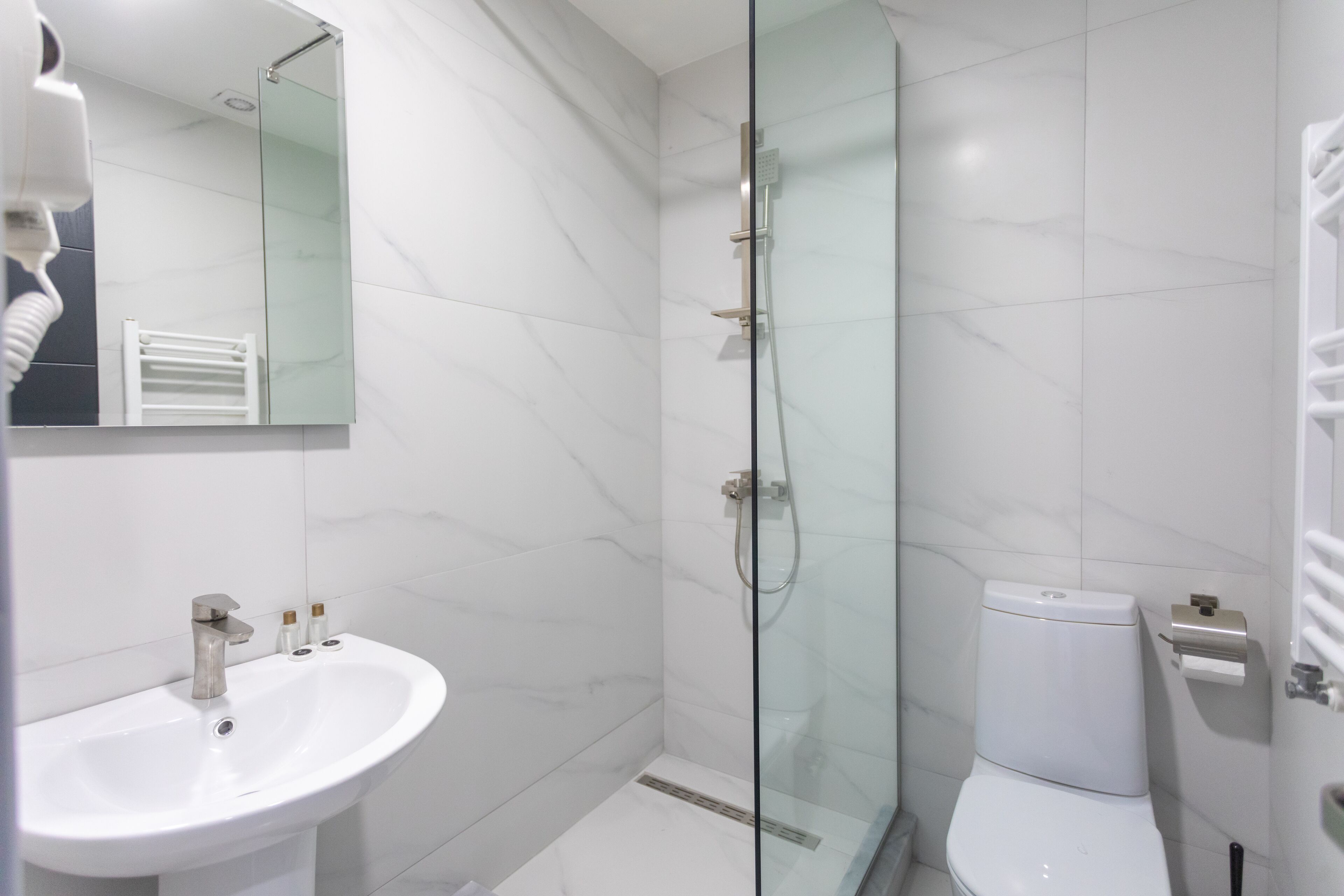 Et moderne badeværelse med en glasvæg omkring brusenichen, en hvid vask og et toilet.