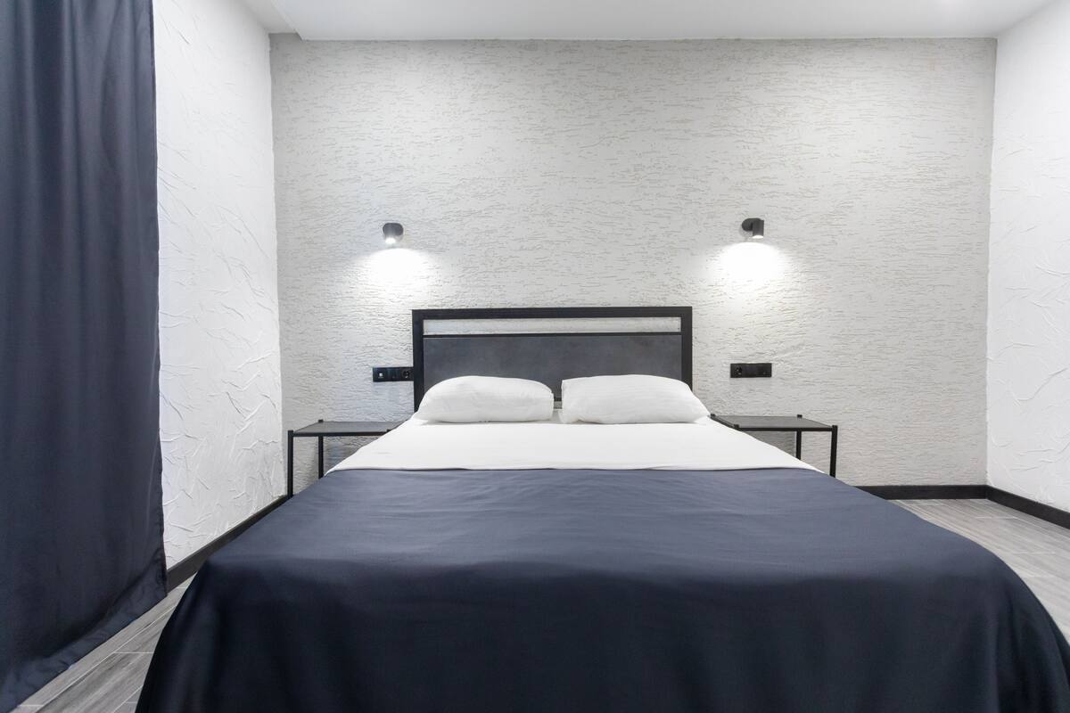 Une chambre d’hôtel moderne avec un grand lit, deux tables de chevet et un mur à texture.