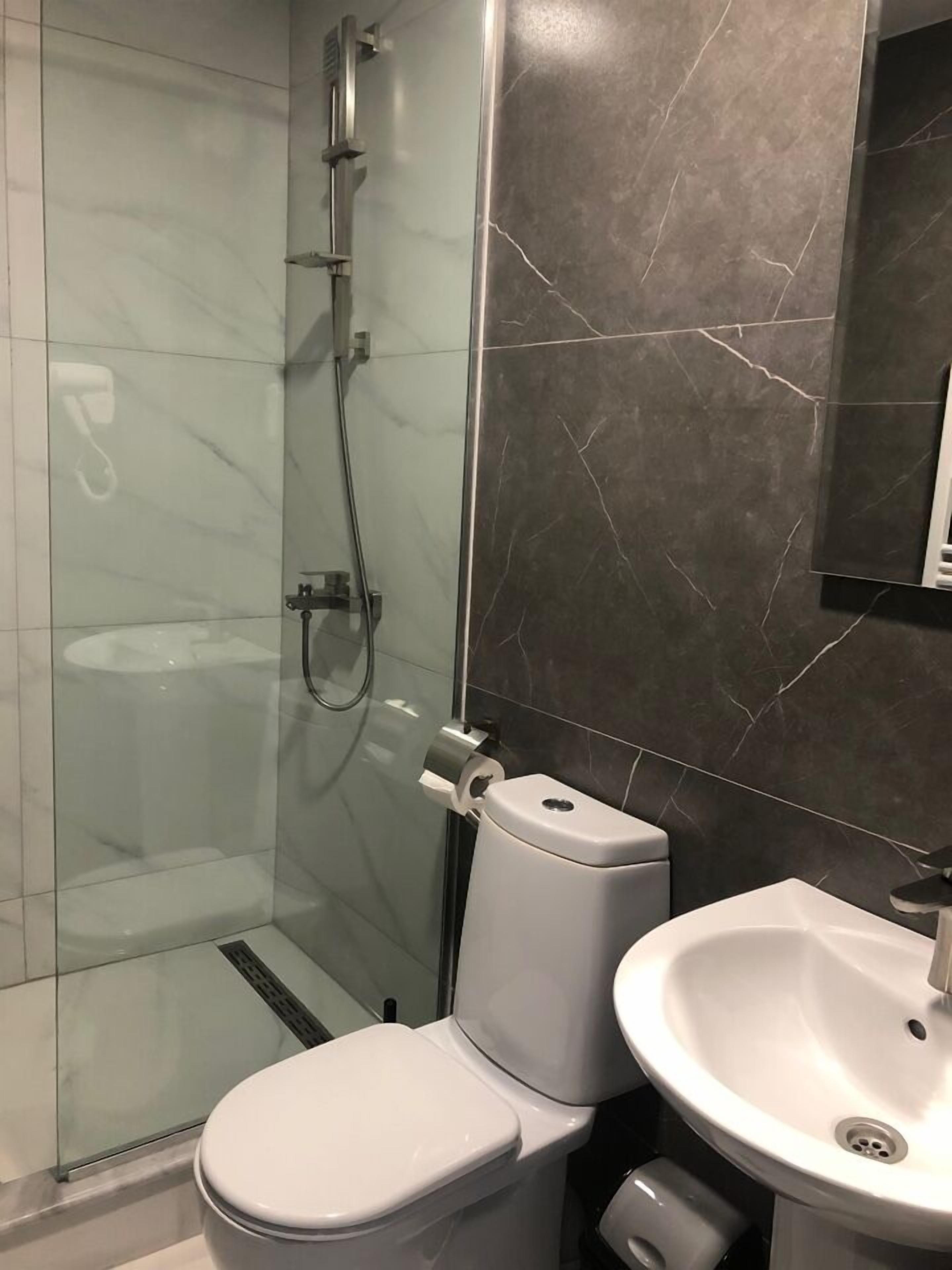 A bathroom with a glass-enclosed shower, a white toilet, and a sink with a mirror above it.