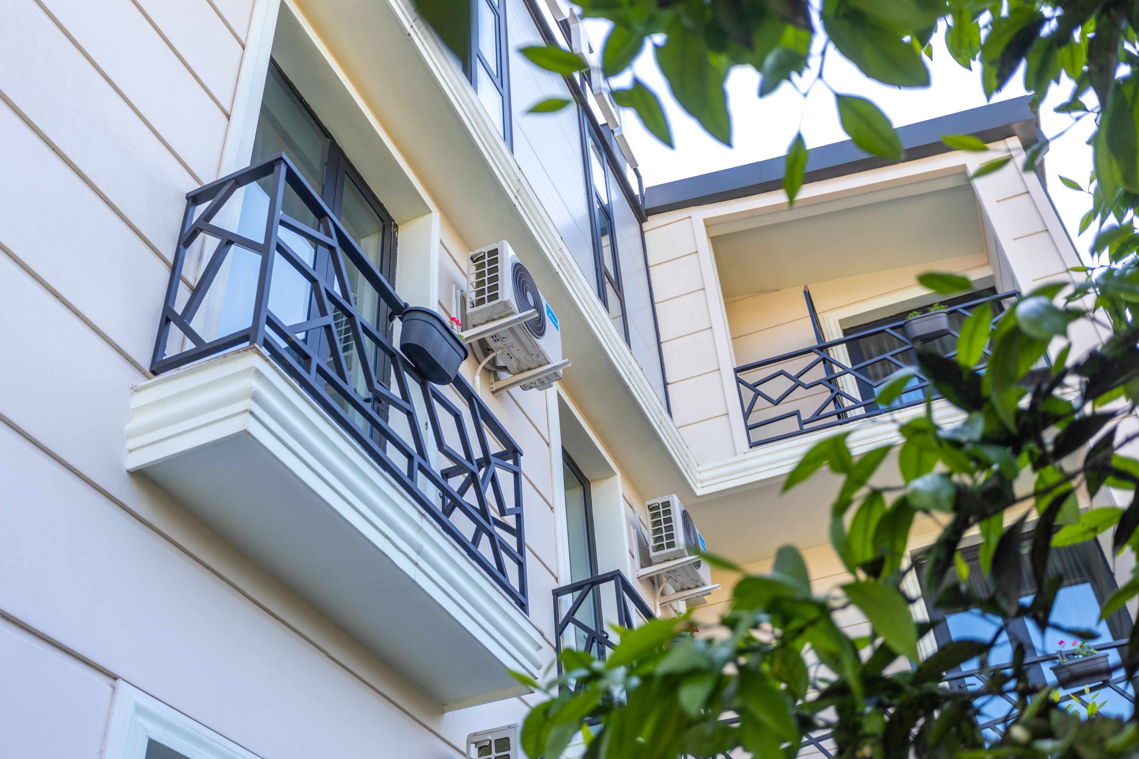 Un edificio de varios pisos con balcones, unidades de aire acondicionado y una ventana con vista al cielo.