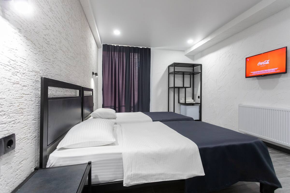 Une chambre d’hôtel avec un lit, un téléviseur fixé au mur et une fenêtre avec des rideaux.