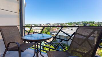 A balcony with two chairs and a small table, overlooking a cityscape with buildings and greenery.