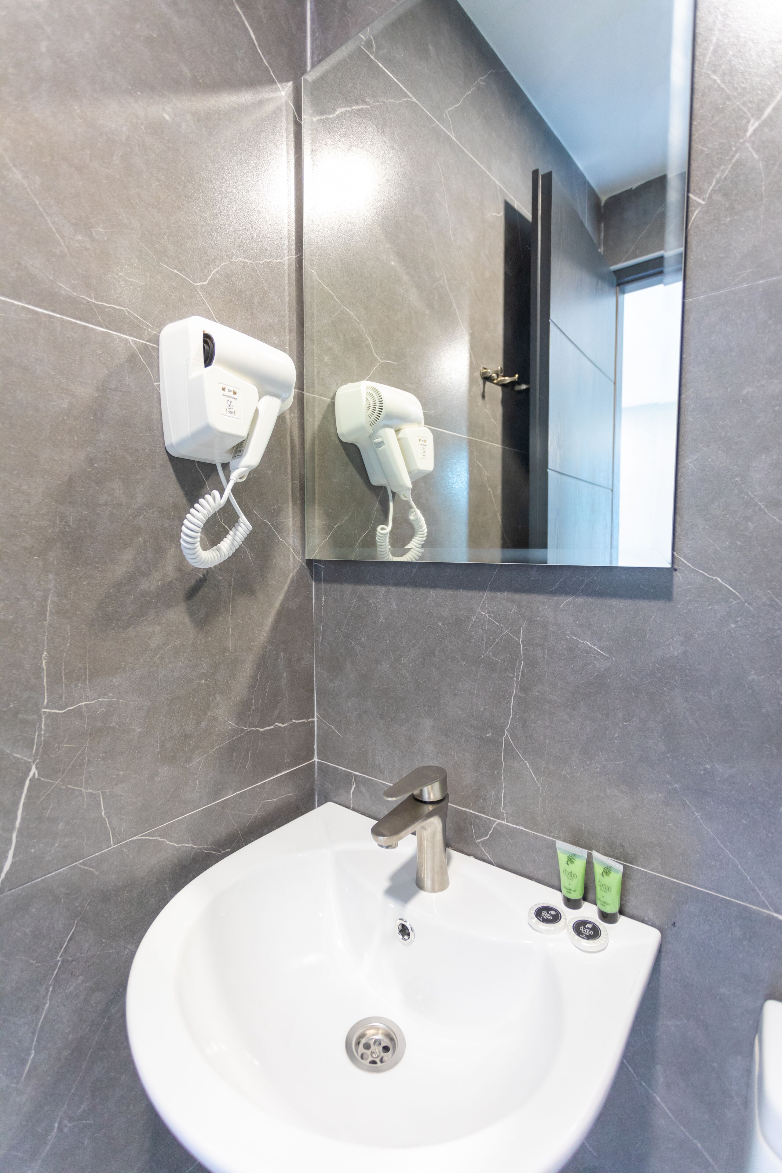 A bathroom with a white sink, a hairdryer mounted on the wall, and a mirror reflecting the room.