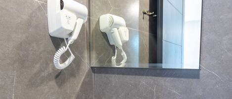 A bathroom with a white sink, a hairdryer mounted on the wall, and a mirror reflecting the room.