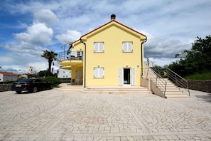 A yellow building with a balcony, a staircase, and a car parked in front.