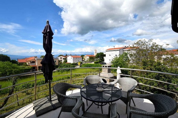 A balcony with wicker furniture, a table, and an umbrella.