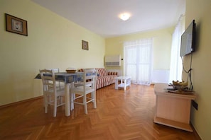 Olohuoneessa on ruokapöytä, tuoleja, sohva, televisio ja patteri.