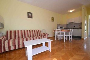 A living room with a sofa and a coffee table, a dining area with chairs and a table, and a kitchen area with cabinets and appliances. - Holiday apartment with balcony and two bedrooms (Milčetići)