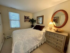 Quarto com cama, cômoda, espelho e janela com persianas.