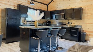 Une cuisine moderne avec des appareils électroménagers noirs, un îlot central doté de tabourets de bar et un revêtement mural en bois.