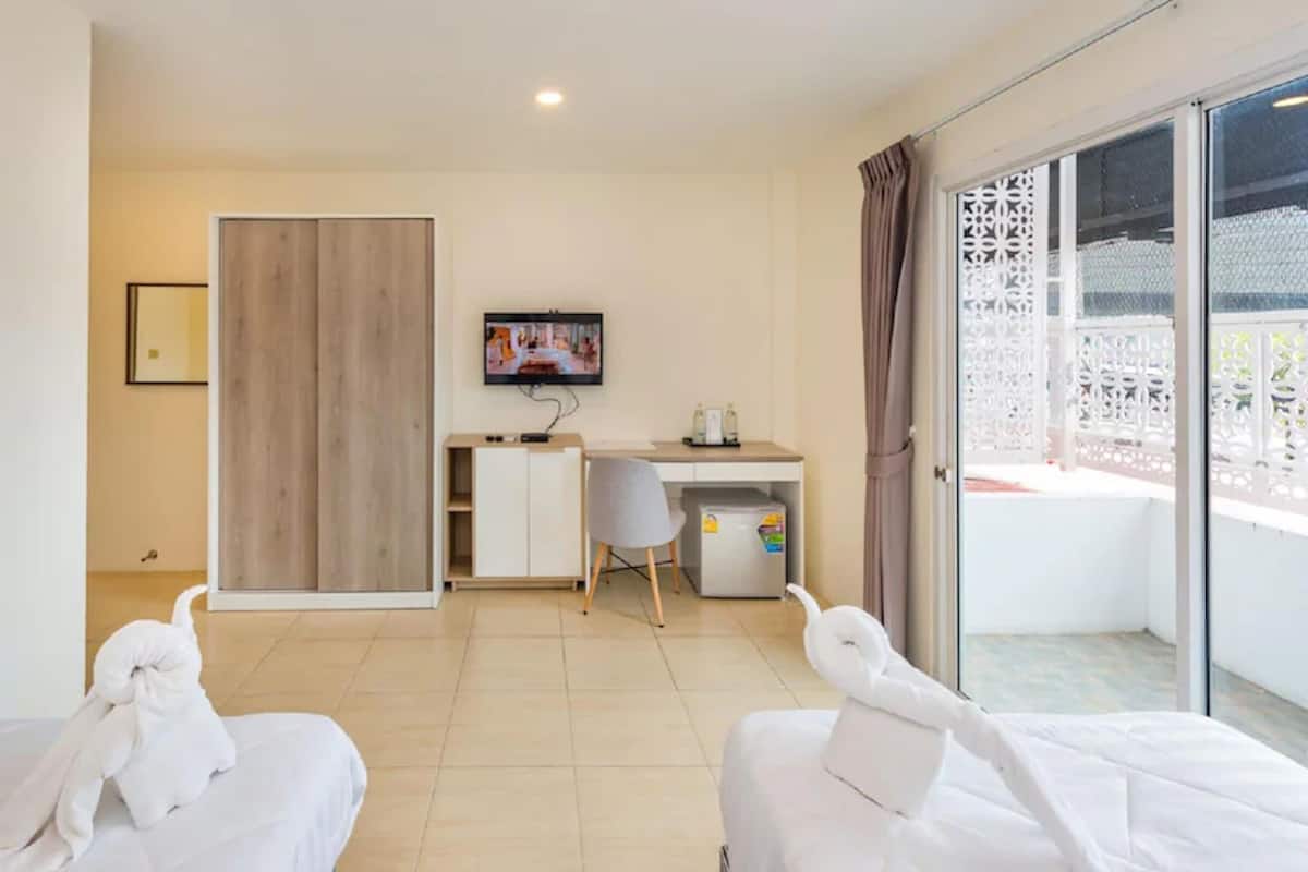 A hotel room with two beds, a desk, a television, and a balcony with a white lattice fence.