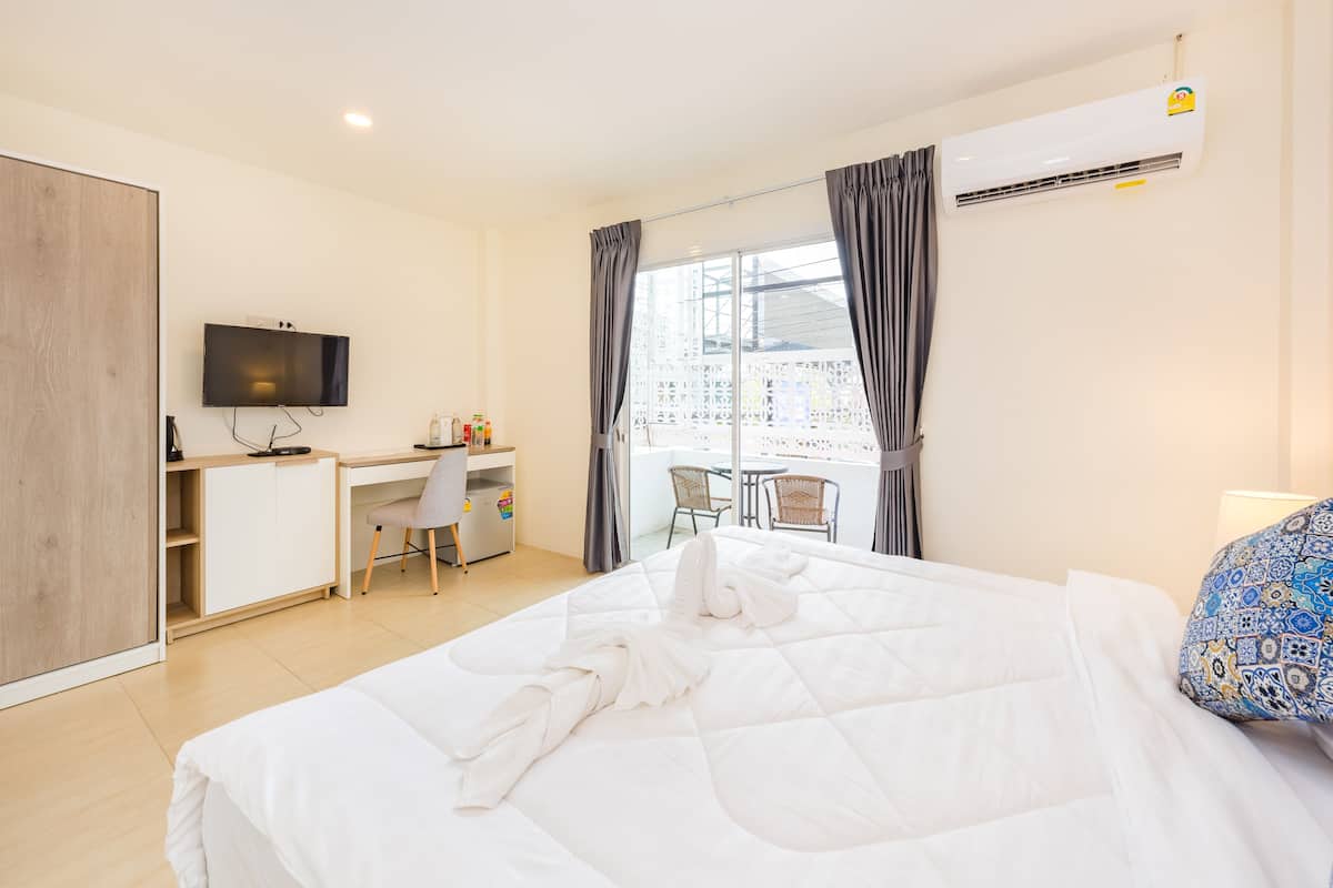 A hotel room with a bed, a desk, a chair, a TV, and a balcony with a view.