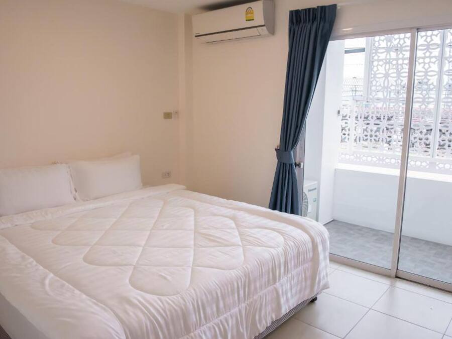 Un dormitorio con una cama grande, un equipo de aire acondicionado y vistas a un balcón con celosía blanca.