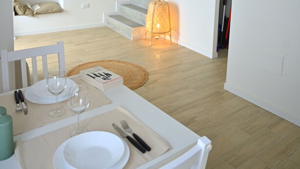 A dining area with a white table set for two, a staircase, and a television mounted on the wall. - Holiday home in historical center a few minutes from the sea.  (Treglio)