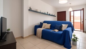 A modern living room with a blue sofa, a flat-screen TV, and a small plant on a dark wooden table. - Elegant two-room apartment with wifi, air conditioning, central area (Sardegna)