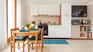 A modern kitchen with white cabinets, a dining table with chairs, and a small bookshelf. - Elegant two-room apartment with wifi, air conditioning, central area (Sardegna)