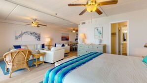 Une chambre spacieuse avec un grand lit, un ventilateur de plafond et une vue sur le salon attenant.